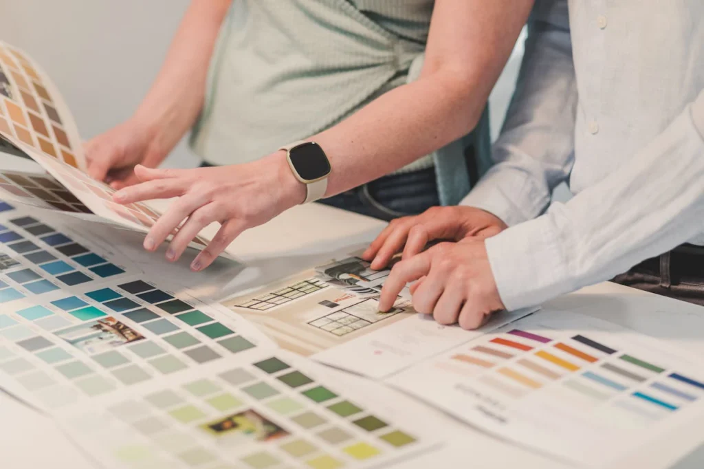 two individuals examining color samples spread out on a table
