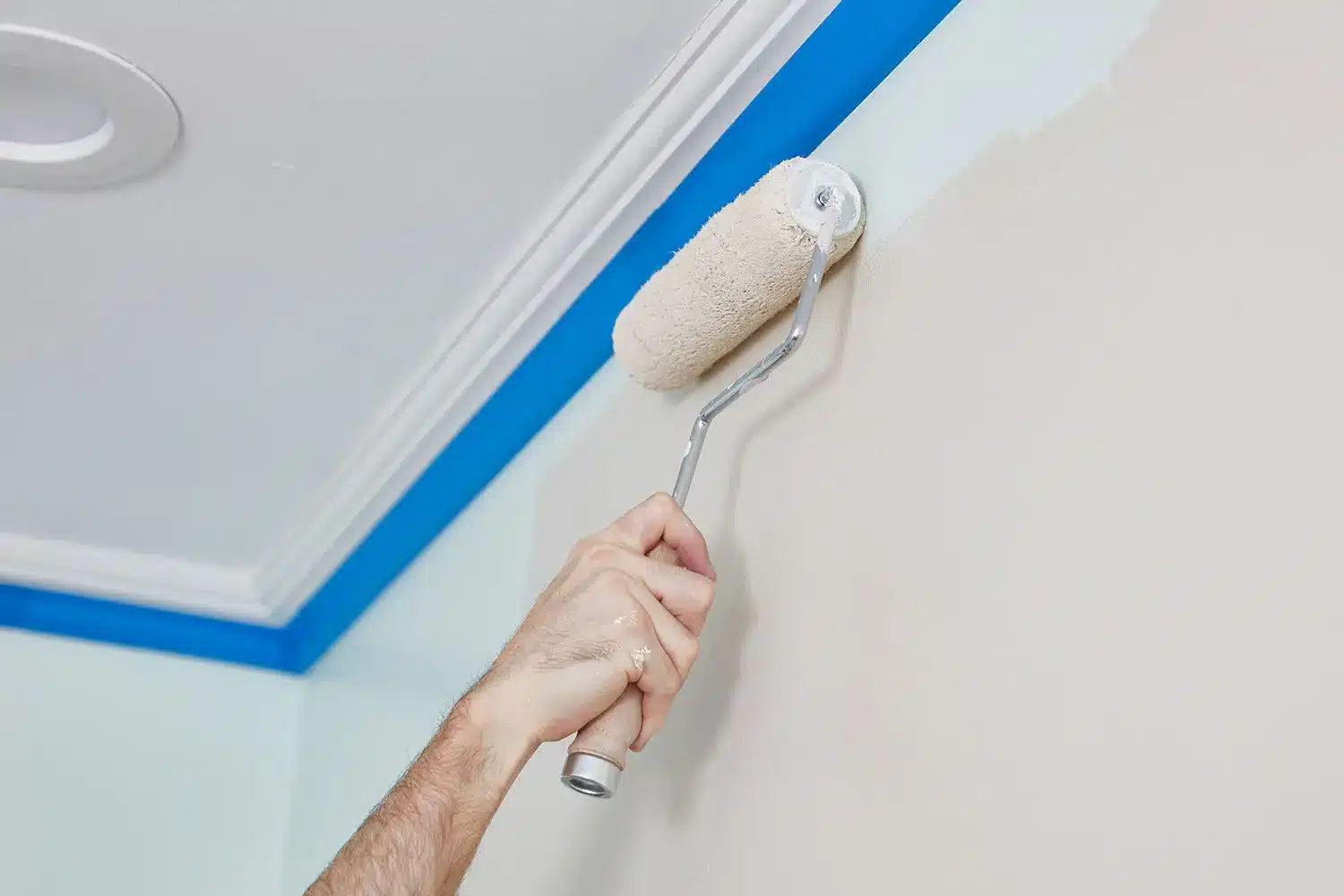 professional painter using roller to apply interior wall paint along taped ceiling edge for clean sharp paint line